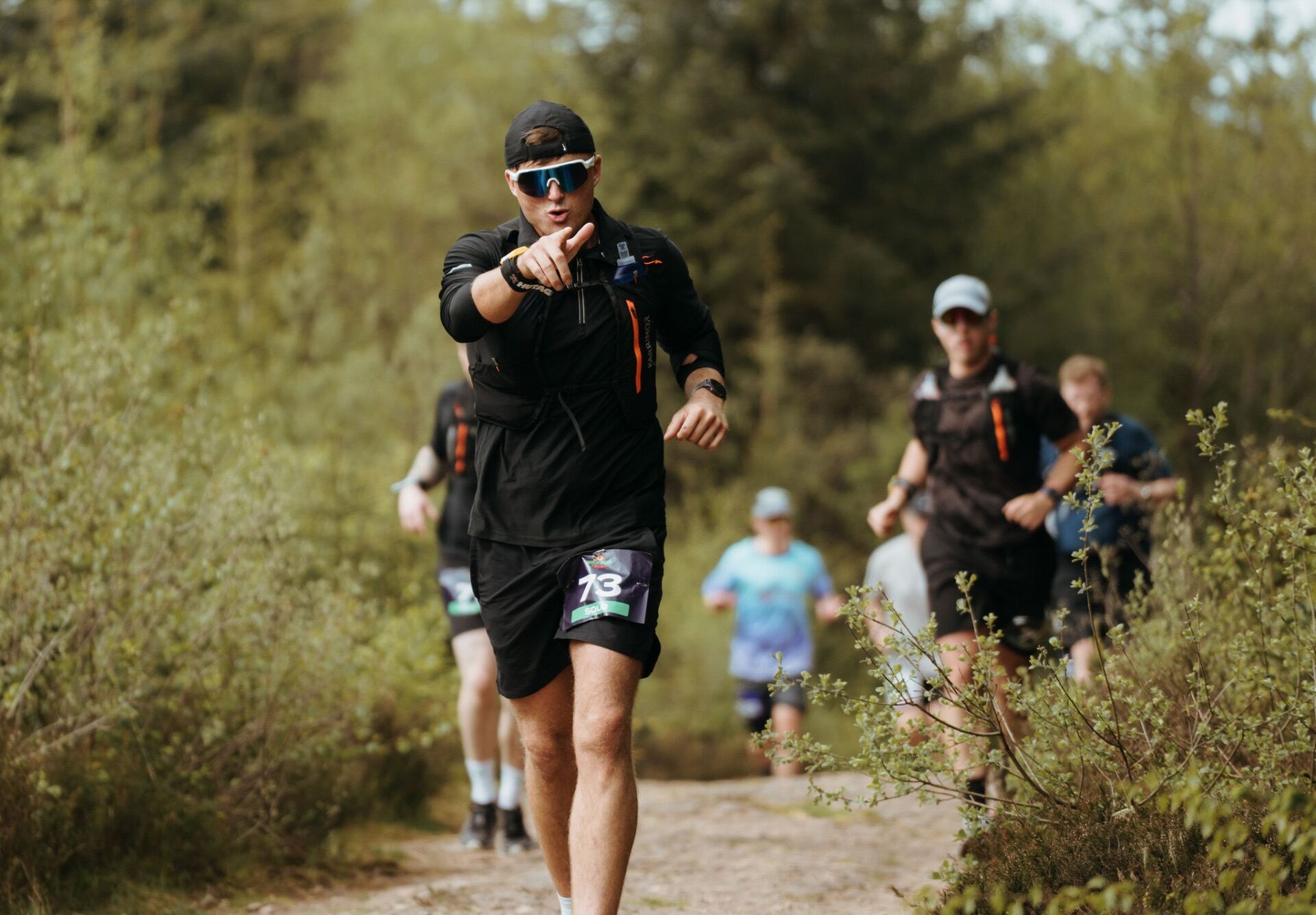 Runner pointing at the camera mid-stride on a woodland trail