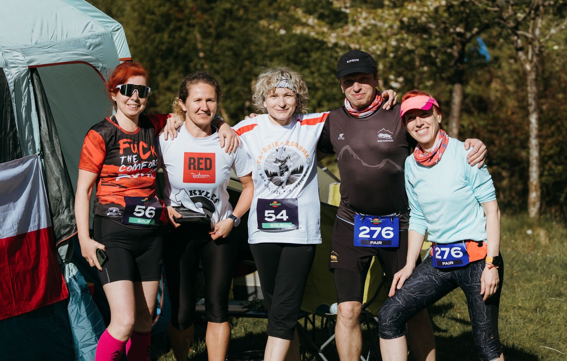 Group of five runners arm in arm posing by their tent in the morning sun