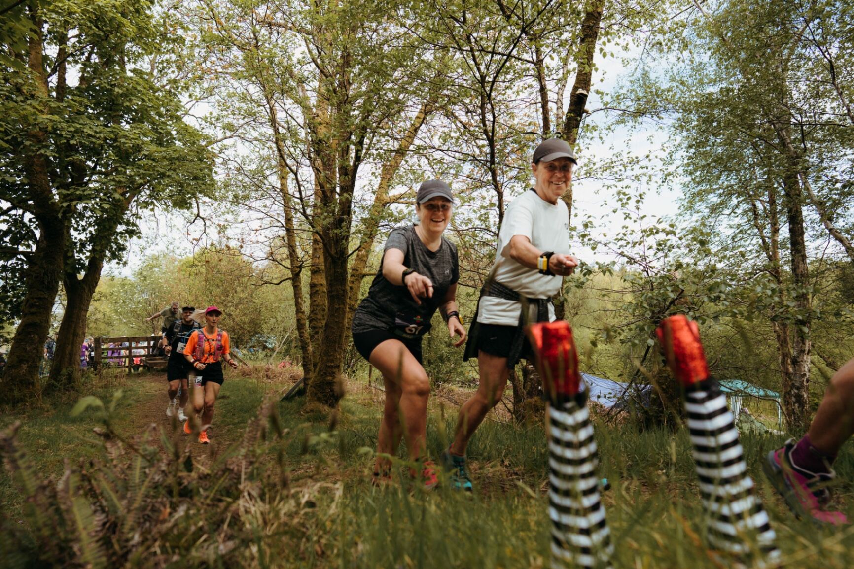 Two runners grinning past witch-leg course markers in the woods
