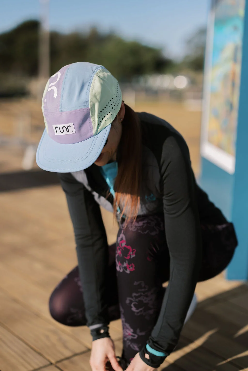 Runner in a pastel Runr five panel cap tying her shoelaces