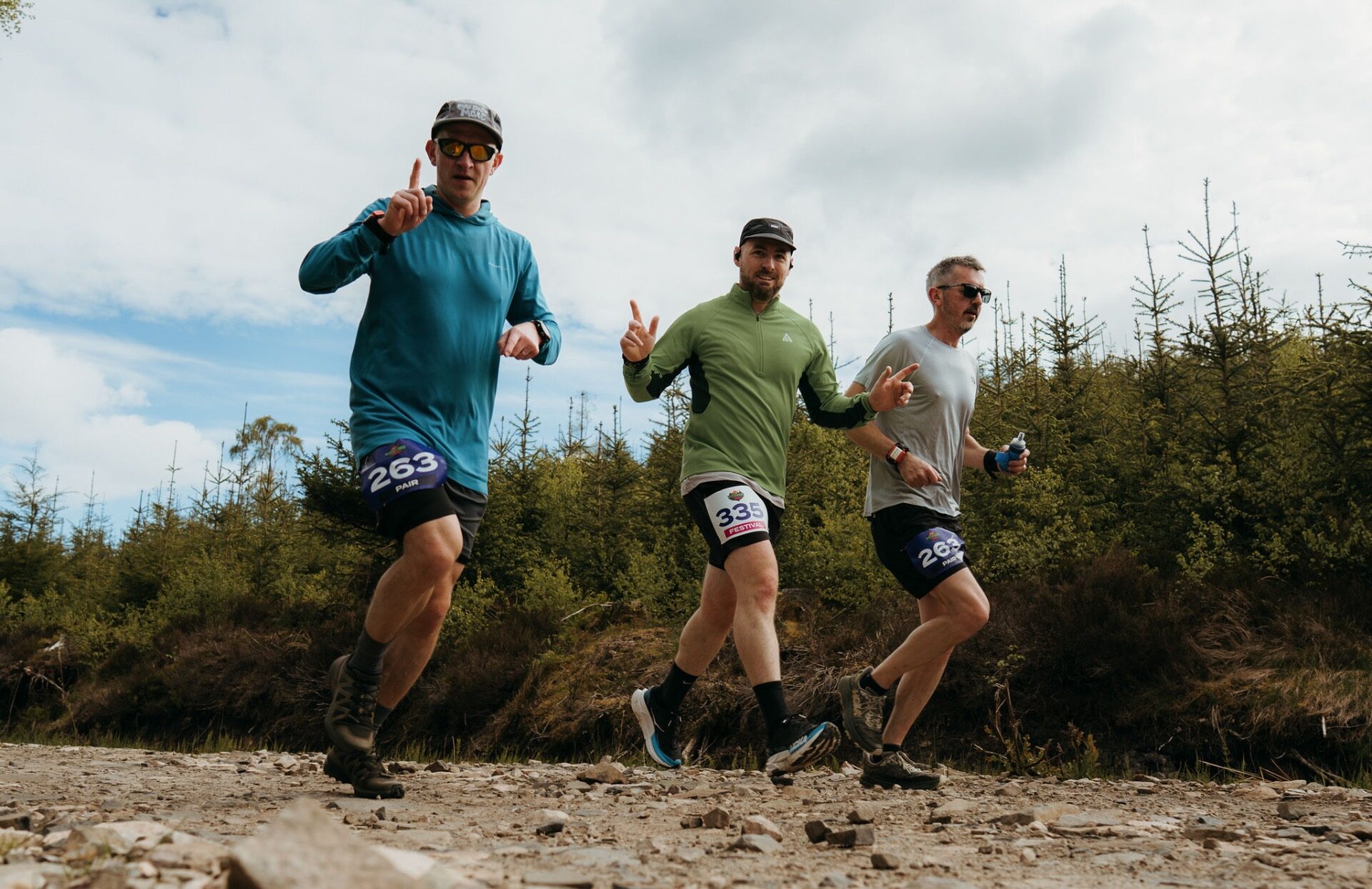 Three runners pointing skyward as they crest a gravel climb