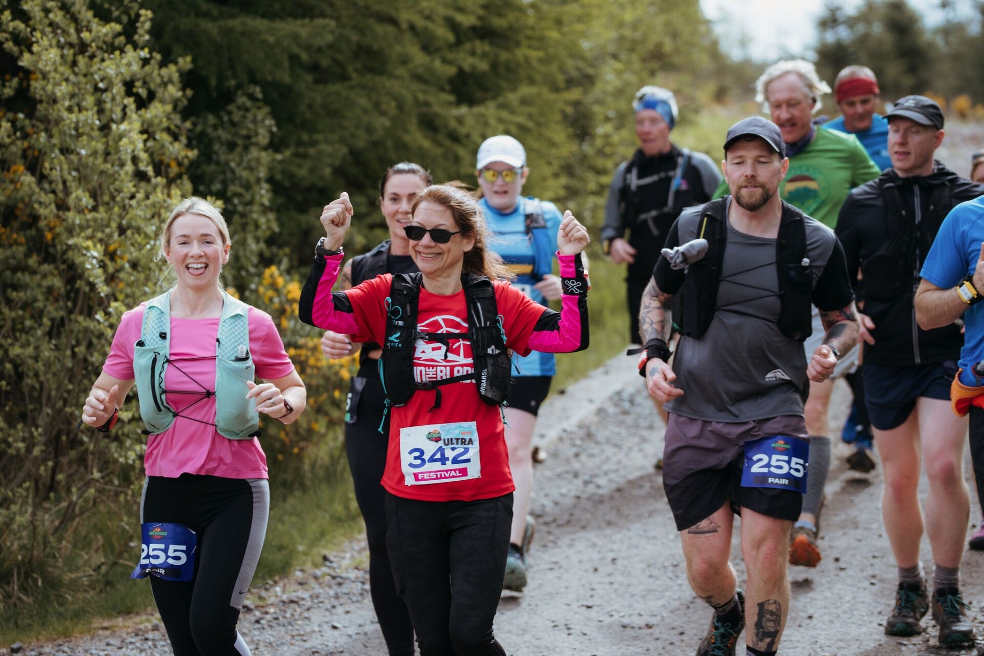 Pack of runners with arms raised heading down the gravel track