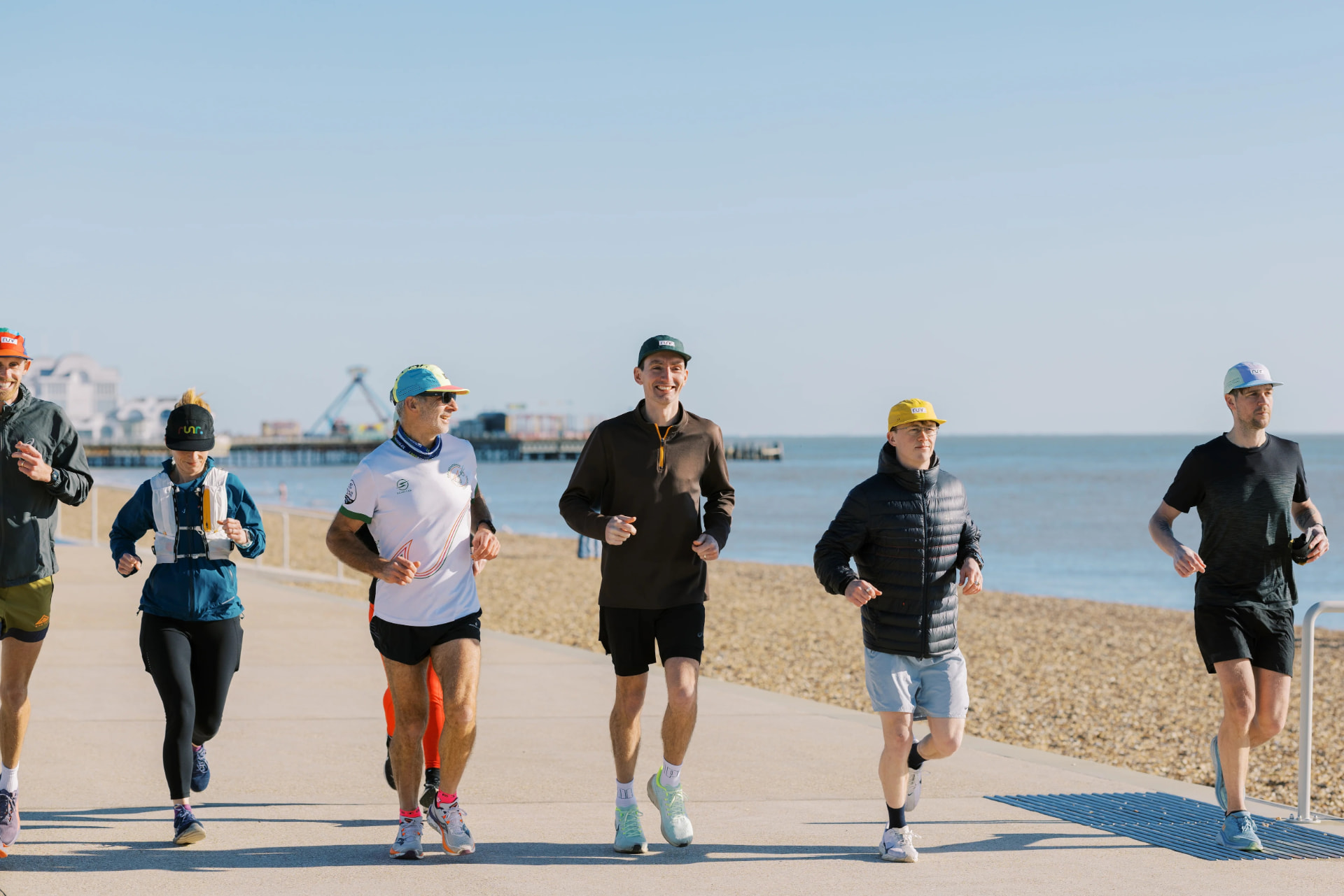 Runners wearing Runr hats along a sunny coastal promenade