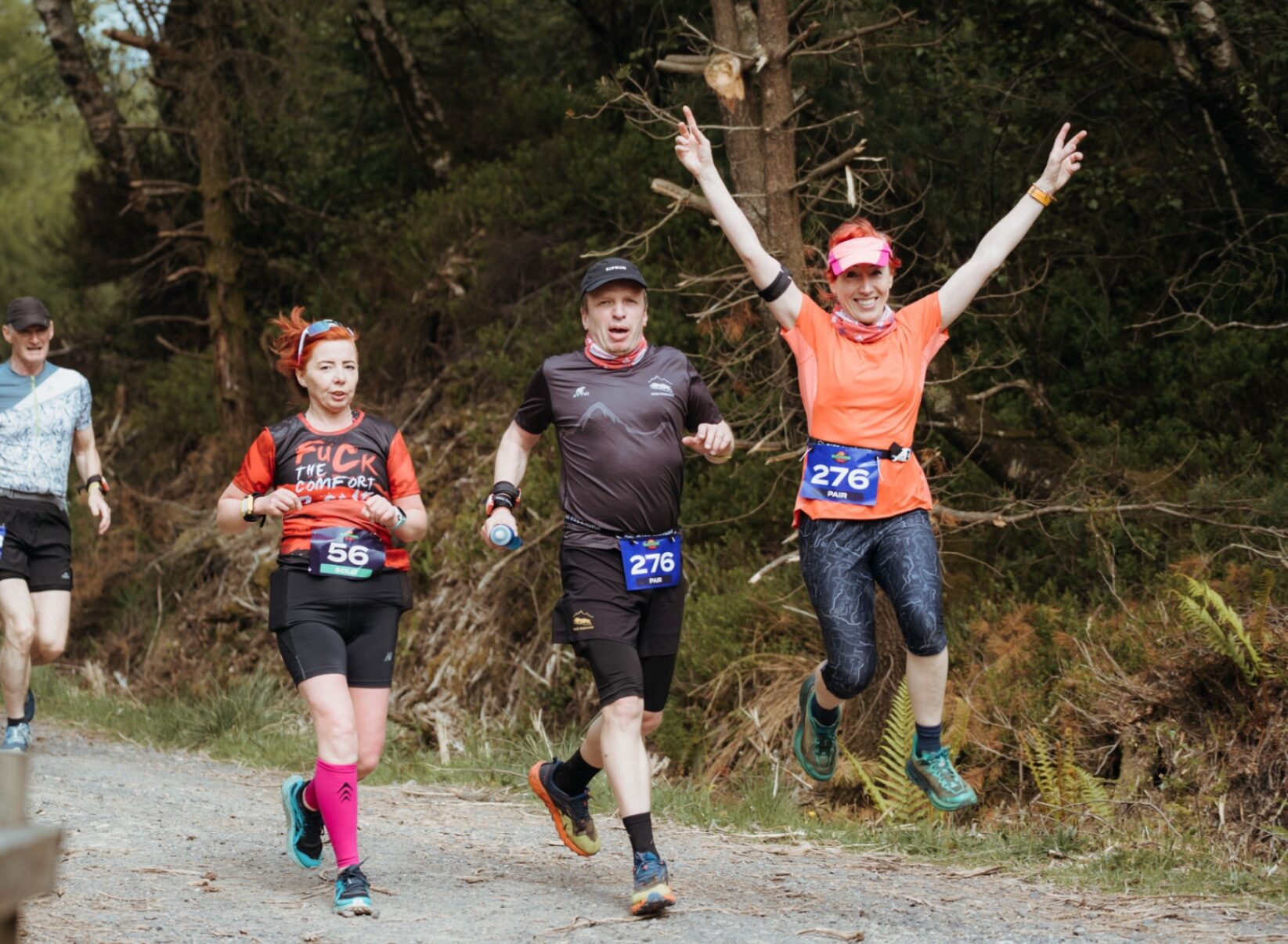Runner jumping with peace signs alongside two others on the trail