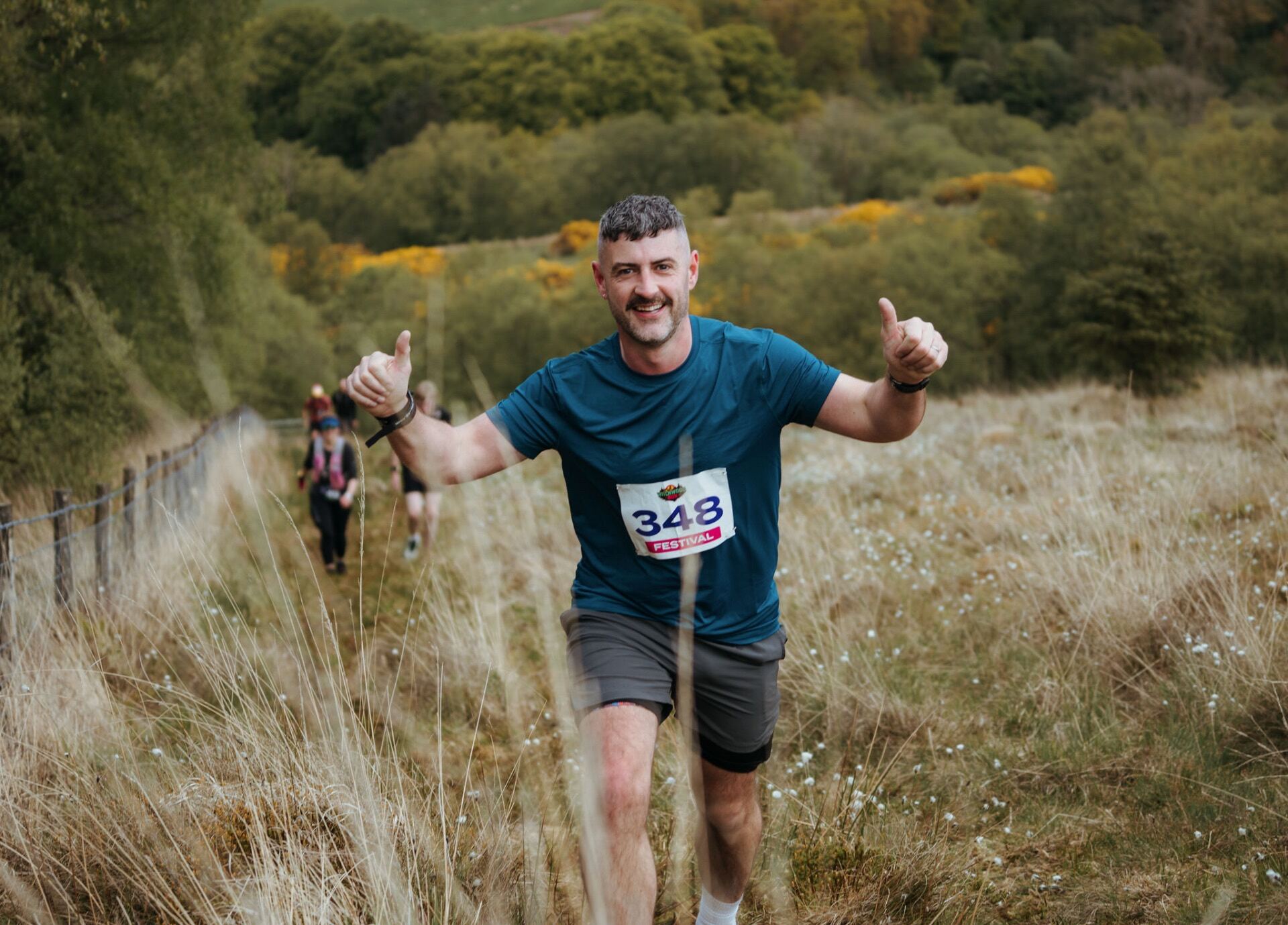 Runner with thumbs up climbing through hillside grass