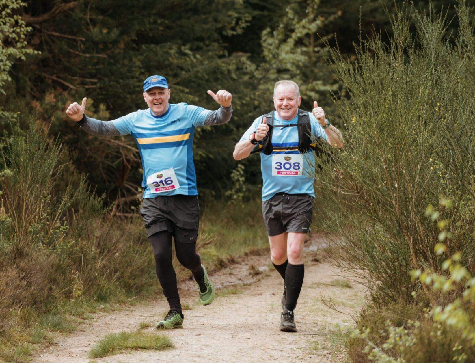 Two runners giving double thumbs up on the forest trail
