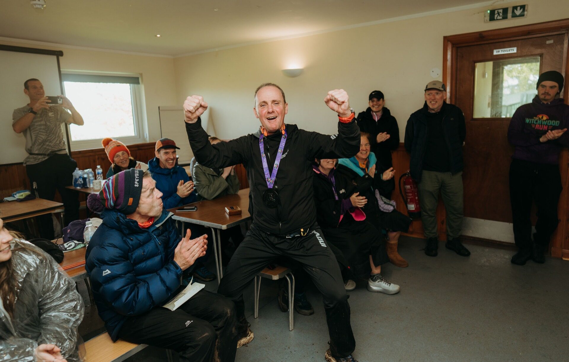 Finisher celebrating with fists raised as the crowd applauds indoors