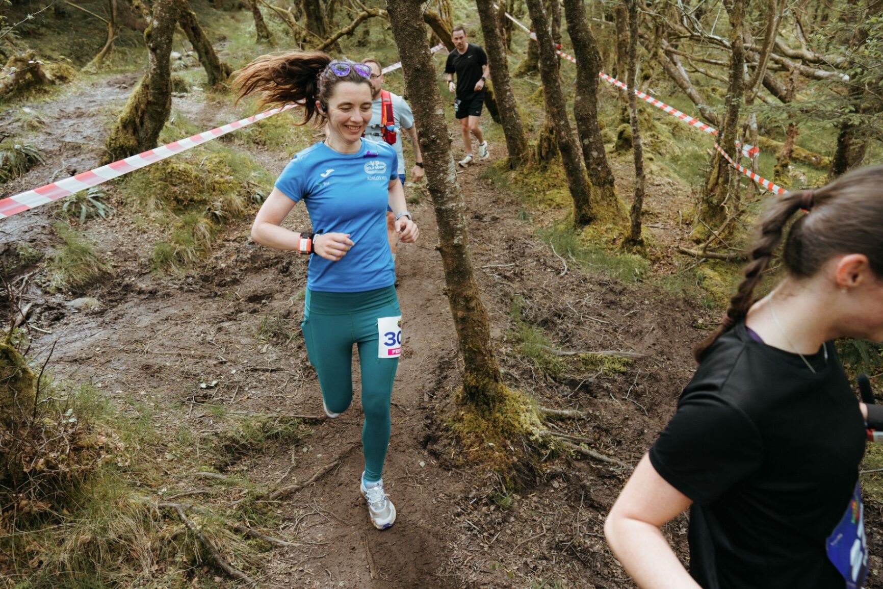 Smiling runner in blue leading a group up a muddy woodland trail