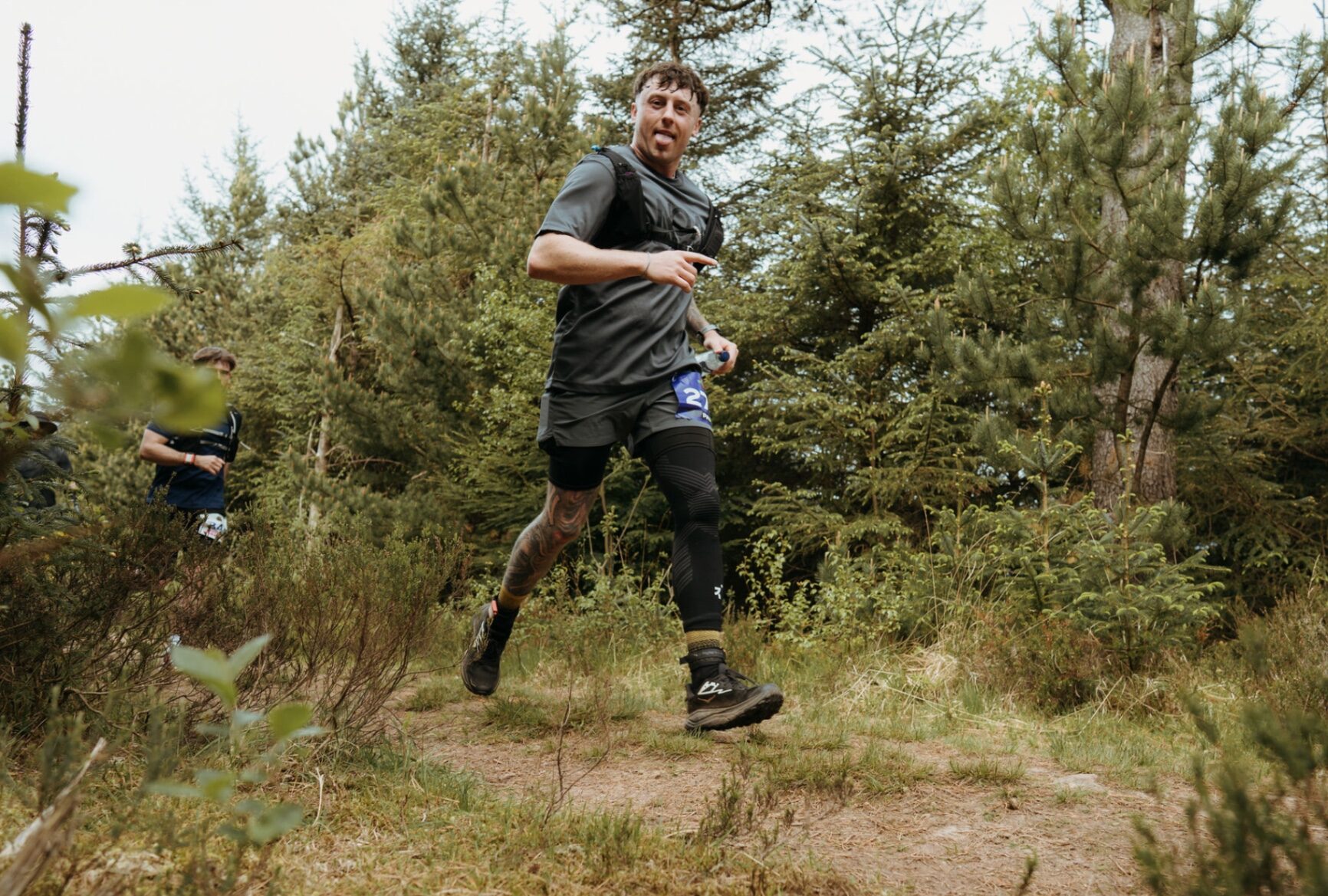 Tattooed runner pointing at the camera on a forest singletrack