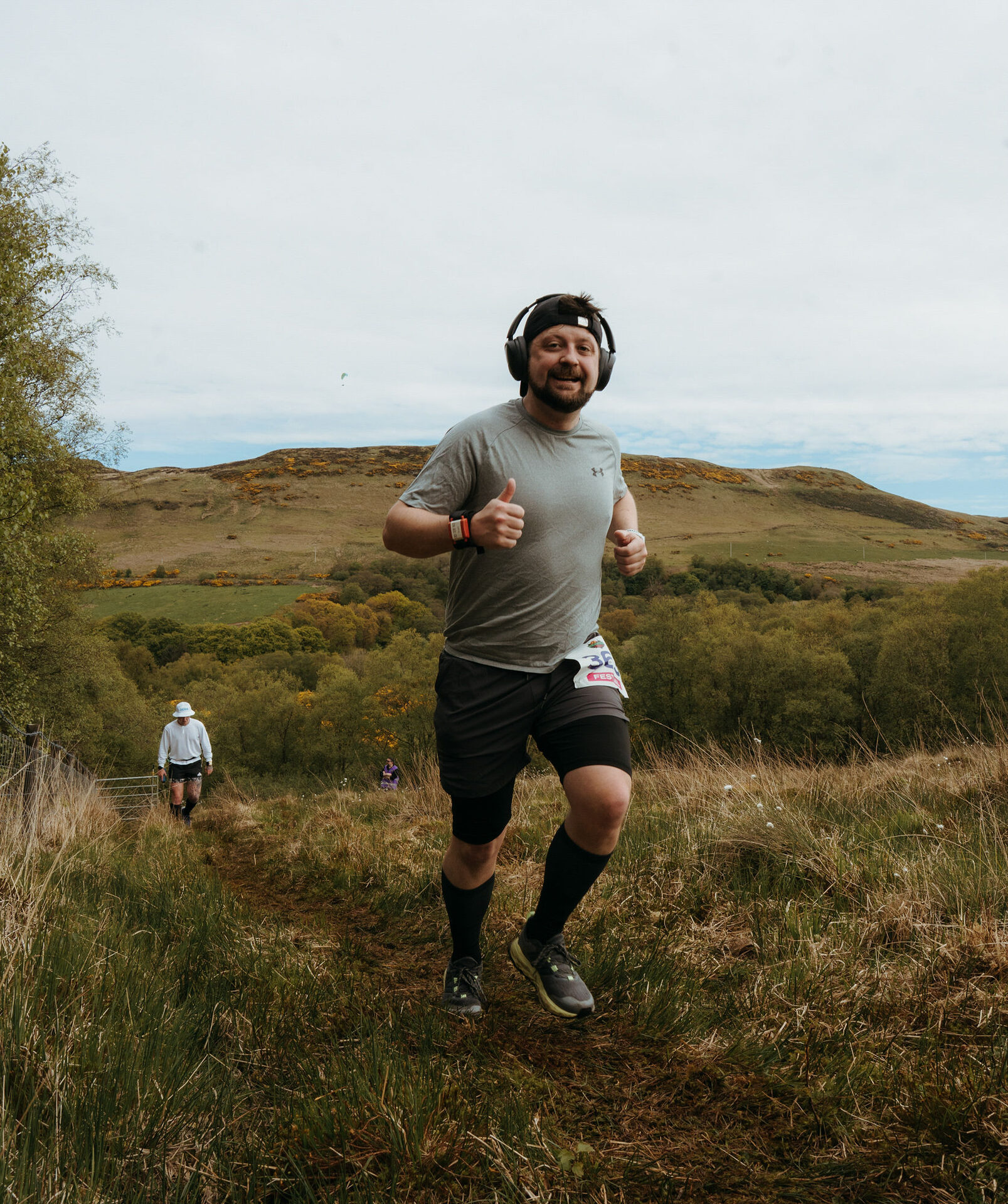 Runner with headphones giving a thumbs up on a grassy hill climb